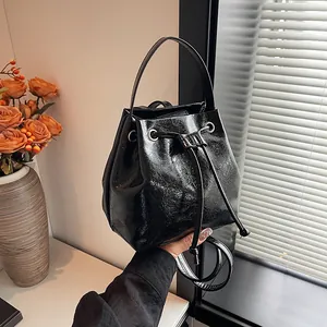 Detail of glossy black patent leather bucket bag with drawstring closure and hand strap