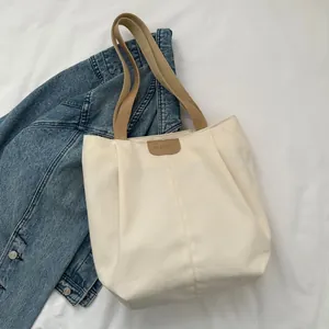 Close-up of cream canvas tote bag featuring brown leather patch and khaki webbed handles