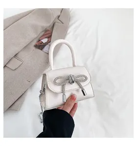Detail of cream mini handbag featuring a sparkling rhinestone bow and silver chain strap