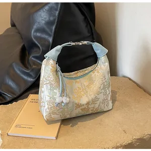 Detail of embroidered brocade dumpling bag with traditional Chinese landscape and blue leather handle