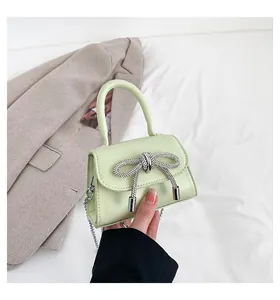 Close-up of light green mini bag with a sparkling rhinestone bow and silver chain strap