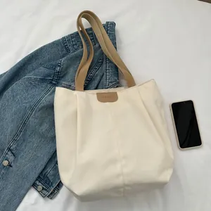 Flat lay of canvas tote bag with brown straps and fashion patch on fabric background