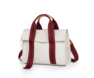 Side view of cream canvas tote bag with striped ribbon handles and leather details