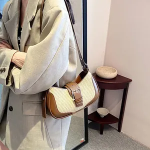 Detail of woven straw and brown leather baguette bag worn with a gray blazer