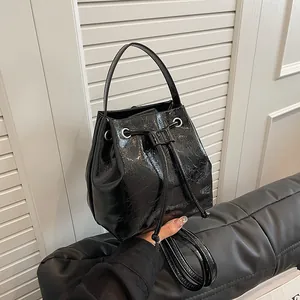 Detail of black drawstring bucket bag with shiny cracked leather texture and silver hardware