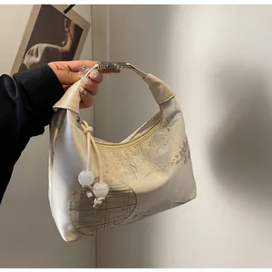 Detail of embroidered floral satin dumpling bag with elegant beaded charm and leather handle