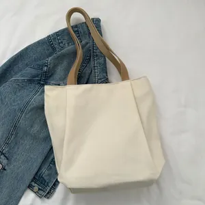 Close-up of cream canvas tote bag with brown leather handles and wide bottom detail