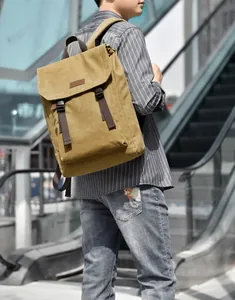 Detail view of khaki canvas backpack with brown straps and buckles on a male model