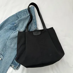 Detail of black canvas tote bag with 'FASHION' leather patch and leather strap