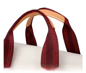 Close-up of canvas tote bag featuring striped webbing handles and brown leather grip