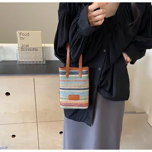 Detalle de un bolso de paja a rayas con adornos de cuero sintético marrón y etiqueta