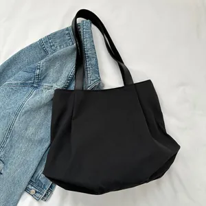 Close-up of black canvas tote bag with wide straps and textured fabric against denim jacket
