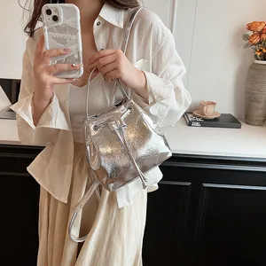 Detail of silver metallic bucket bag with drawstring and crinkle texture held by a model