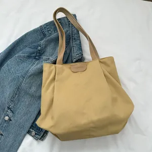 Detail of khaki canvas tote bag featuring brown leather patch with FASHION engraving