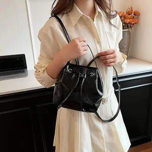 Fashionable black patent leather bucket bag with drawstring closure and silver eyelets detail