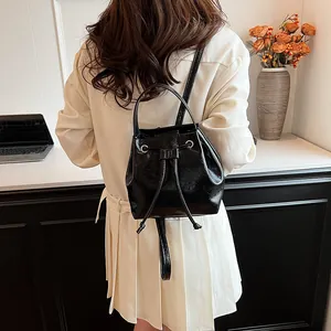 Detail of a shiny black drawstring bucket backpack shown on model with polished finish