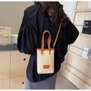 Detalle del bolso de paja tejido con asas de cuero marrón y una correa de hombro chic