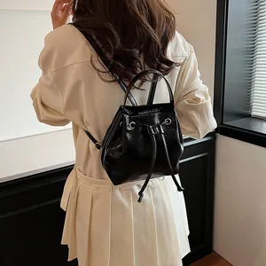 Mini black glossy backpack shown from side-rear view on model with drawstring closure