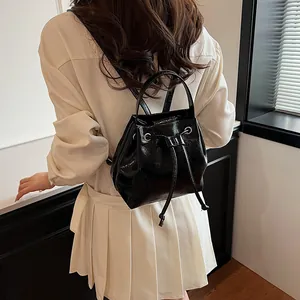 Detail of black patent leather bucket backpack featuring drawstring closure and top handle