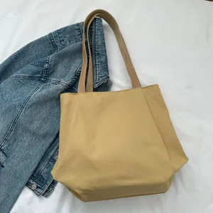Detailed top view of large khaki canvas tote bag on white fabric with denim jacket