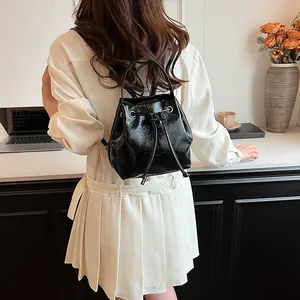 Model showing the back view of a black glossy leather bucket backpack with drawstring