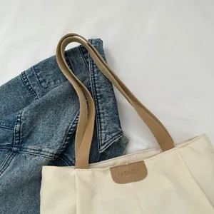 Detail of off-white canvas tote bag featuring brown fashion label and fabric handles