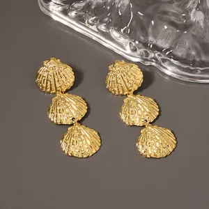 Three-tier gold shell drop earrings with textured metal finish on a grey surface