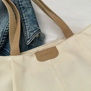 Close-up of cream canvas tote bag featuring brown leather trim and embossed fashion logo