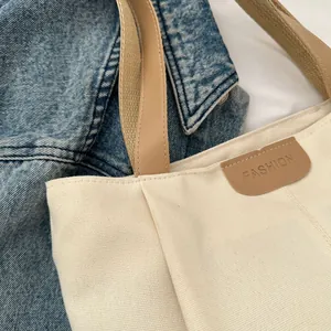 Close-up of off-white canvas tote bag with brown leather strap and FASHION embossed tag