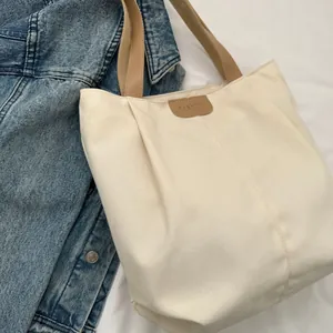 Flat lay of cream canvas tote bag with brown leather accents next to denim jacket