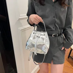 Metallic silver drawstring bucket bag with pleated texture shown as a handbag and crossbody