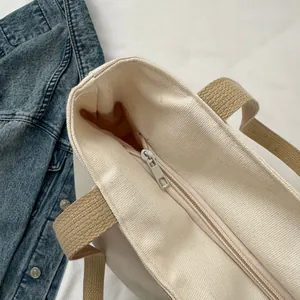 Detail view of canvas tote bag showing metal zipper closure and woven handles