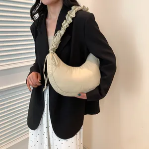 Elegante borsa a mezzaluna beige plissettata indossata a spalla da una modella chic