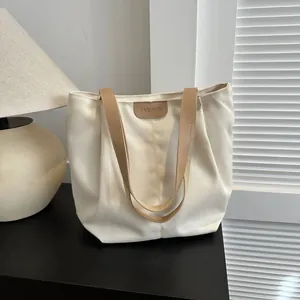 Close-up of beige canvas tote bag with brown leather straps and FASHION embossed patch