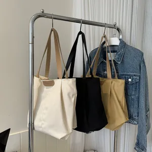 Three large canvas tote bags in white black and khaki hanging on a silver metal rack