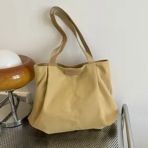 Detail of a large yellow canvas tote bag with a leather Fashion label and tan straps