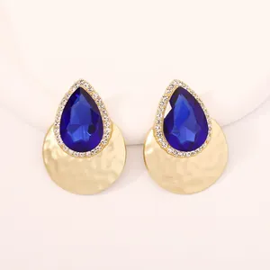 Dettaglio di orecchini a goccia con pietre blu scuro e finitura dorata martellata