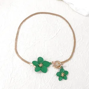 Detail of elegant gold flat snake chain necklace with green flower pendant and toggle clasp