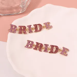 Makroaufnahme goldener BRIDE Ohrhänger mit funkelnden rosa Kristallen auf Keramik