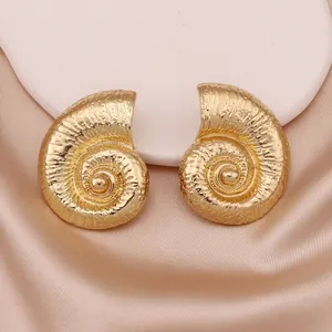 Elegant gold spiral conch shell stud earrings displayed on a luxury silk fabric background