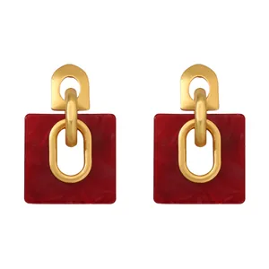 Detalle macro de pendientes geométricos con resina jaspeada roja y ganchos dorados