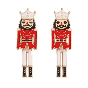 Pair of festive Nutcracker soldier earrings with red and gold enamel on white background