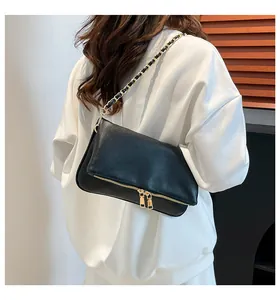 Detail of black pebbled leather crossbody bag with gold zippers worn by model