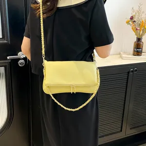 Pale yellow leather crossbody bag with chain strap shown on model in a modern interior