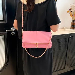 Pink faux leather crossbody bag with gold chain strap shown on model in a modern interior