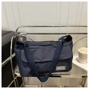 Detail of navy blue messenger bag with adjustable strap and fashion label on flap