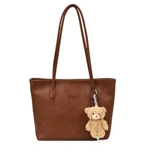 Brown faux leather tote bag with vintage texture and plush bear pendant accessory