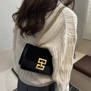Schwarze Umhängetasche aus Leder mit goldener G-Schnalle und Kette auf weißem Pullover
