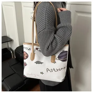 Close-up of white canvas tote bag with astronaut print and light brown shoulder strap