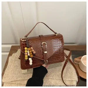 Close-up of brown crocodile texture handbag with decorative wooden beads and gold buckle